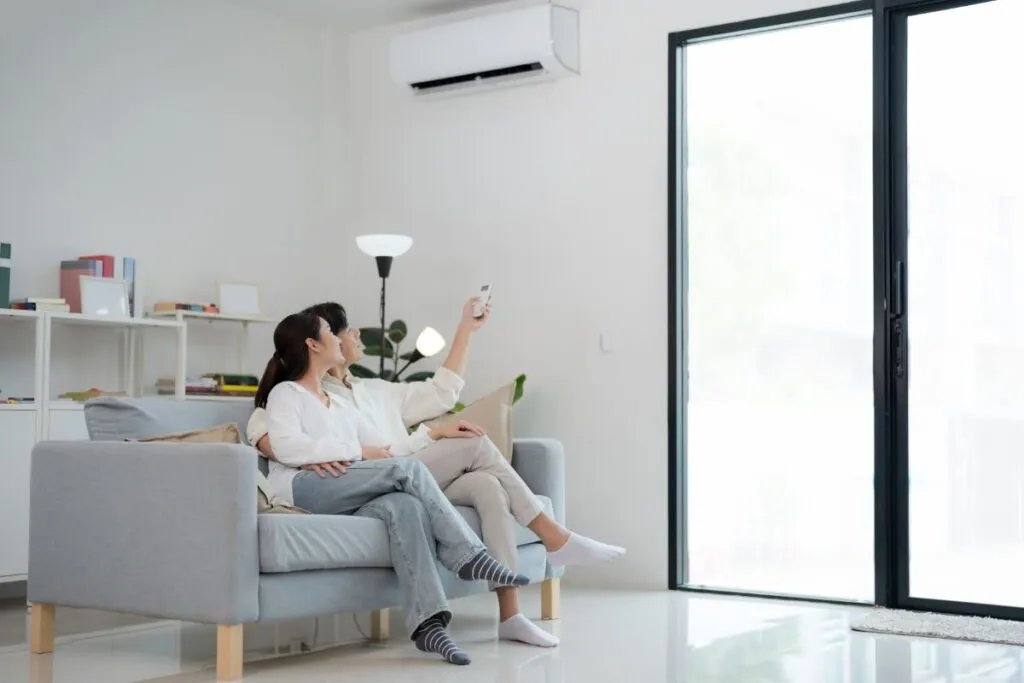 couple relaxing on couch adjusting air conditioner with remote